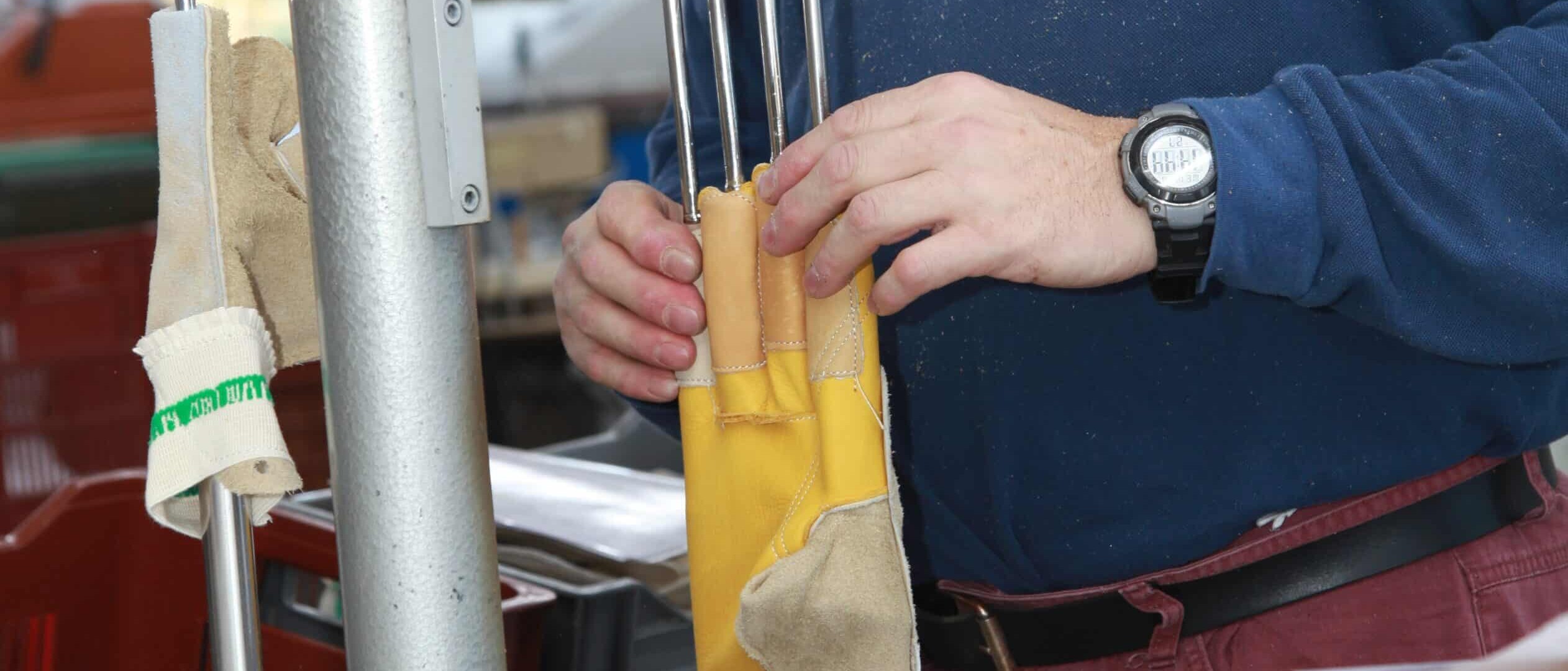 Un artisan ajuste un gant en cuir jaune et beige sur un moule métallique chauffant pour lui donner sa forme finale dans un atelier de fabrication.